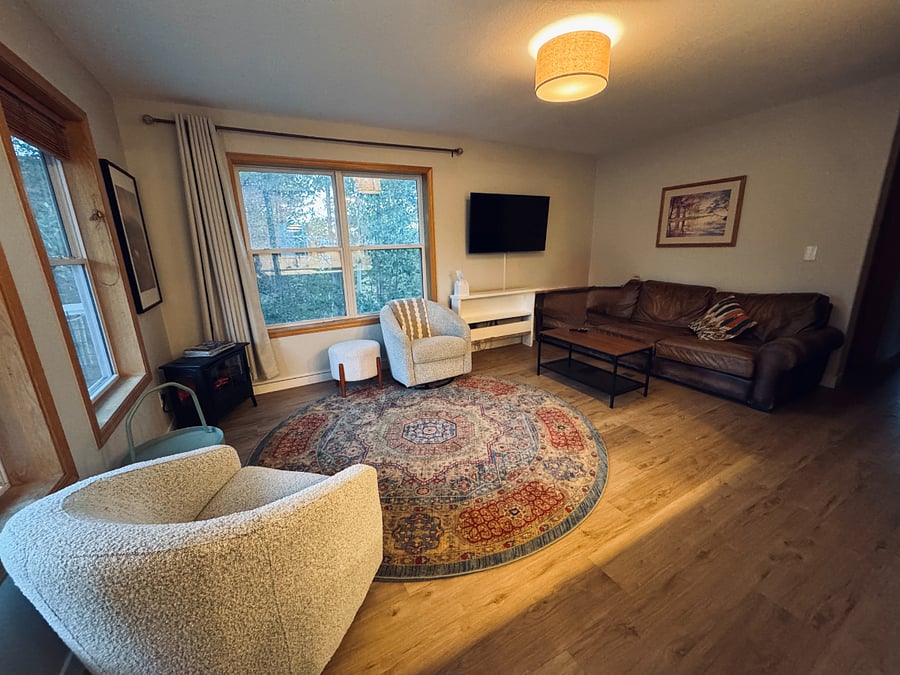 Living room features lots of natural light and trees outside of windows.