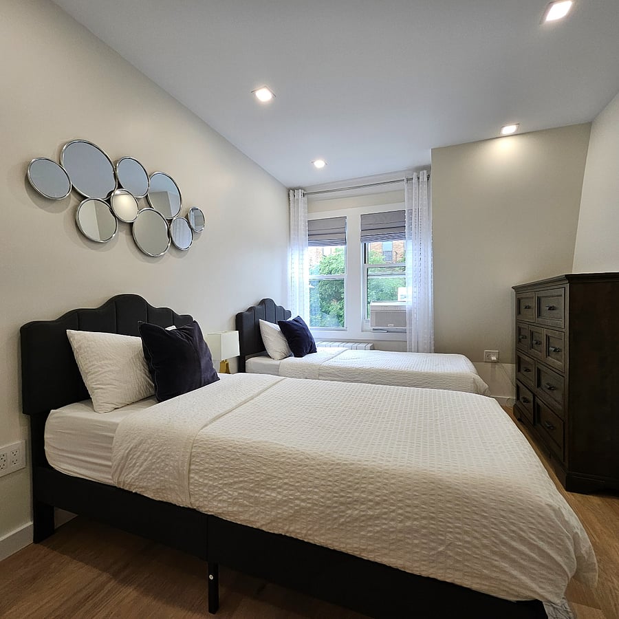 Cozy second bedroom with two single beds, tall dresser, and blackout curtains for restful sleep. 