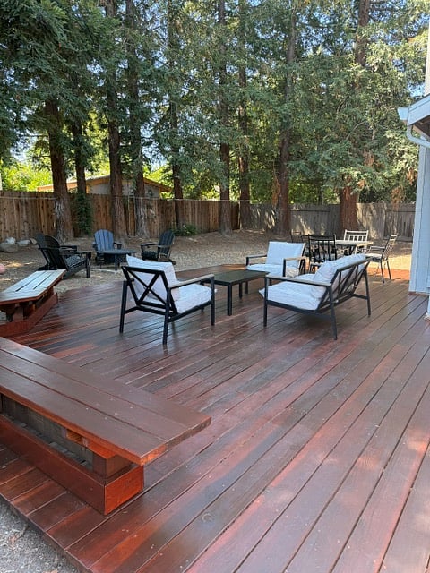 Spacious furnished deck with multiple seating areas beneath mature trees.