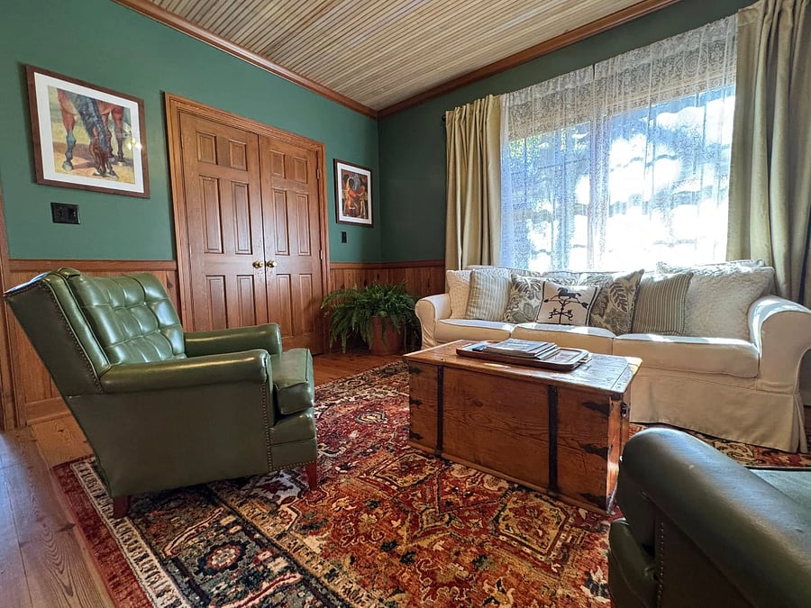 The living room has a comfortable sofa, an antique wooden chest, vintage leather chairs, a smart TV, and art by an award-winning local painter. 