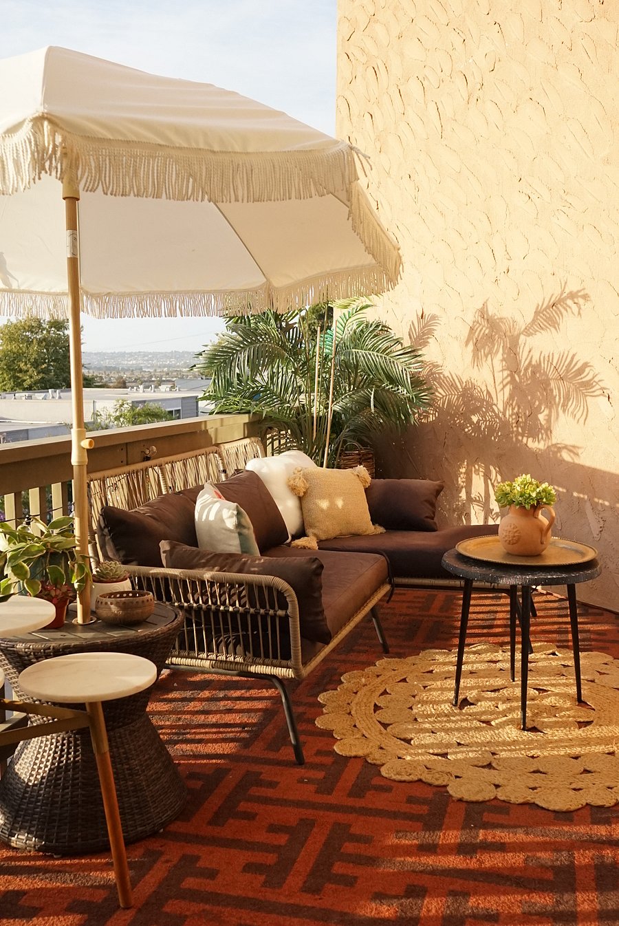 Close-Up of Main Common Area Balcony. Featuring an L-Shaped Outdoor Sofa, Boho Patio Umbrella, Outdoor Rug, variety of plants, and views of both SeaWorld as well as the waters of Ocean Beach. 