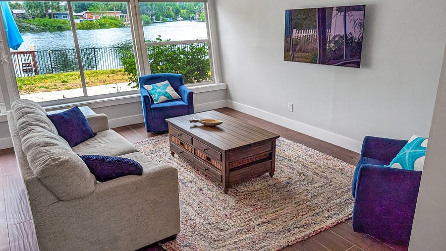 Open concept main living area bathed in natural light featuring comfortable seating and peaceful framed views of the water.