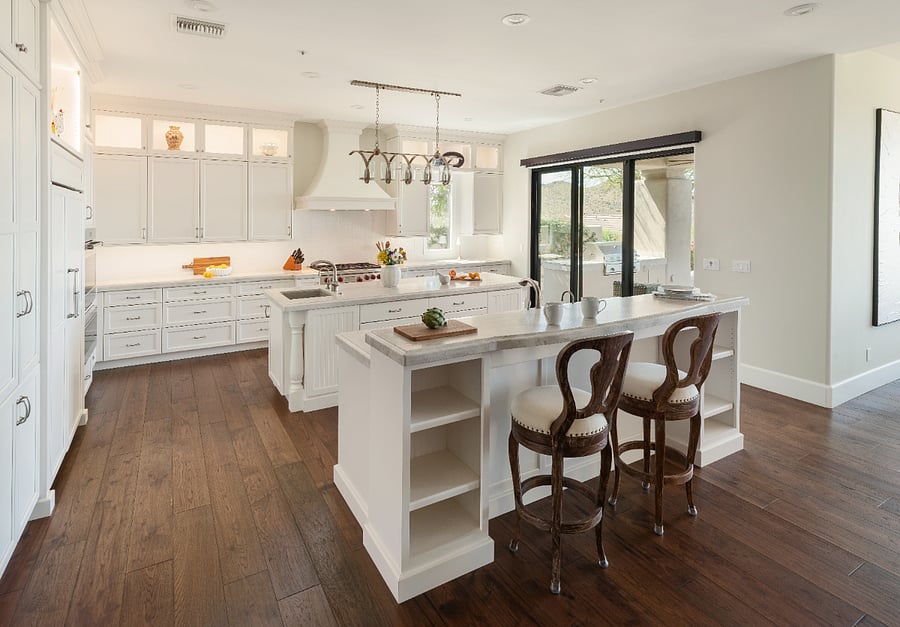 The chef's kitchen features two large islands with stone countertops, a professional-grade range, custom white cabinetry to the ceiling, and more storage than you'll know what to do with. The bar seating and slider to the outdoor patio make it the natural heart of the home.