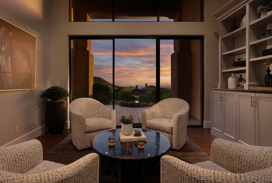 A dedicated sitting area with four swivel chairs, a marble top coffee table, and floor-to-ceiling sliding doors that frame unobstructed views of Troon Mountain and city lights at sunset.