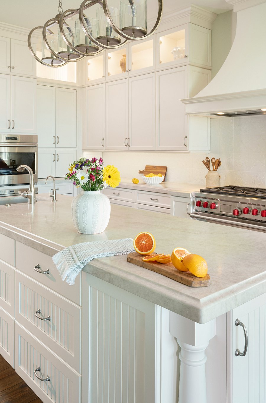 The chef's kitchen features two large islands with stone countertops, a professional-grade range, custom white cabinetry to the ceiling, and more storage than you'll know what to do with. The bar seating and slider to the outdoor patio make it the natural heart of the home.