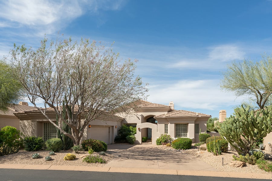 Single-level Southwestern-style home in a gated North Scottsdale community with a circular driveway, two-car garage, arched entry, and mature desert landscaping.