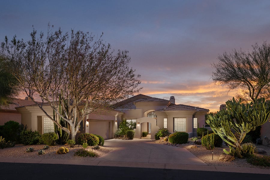 3,600 square foot single-level home in a gated Troon Mountain community, lit at dusk with Sonoran desert landscaping and an arched courtyard entry.