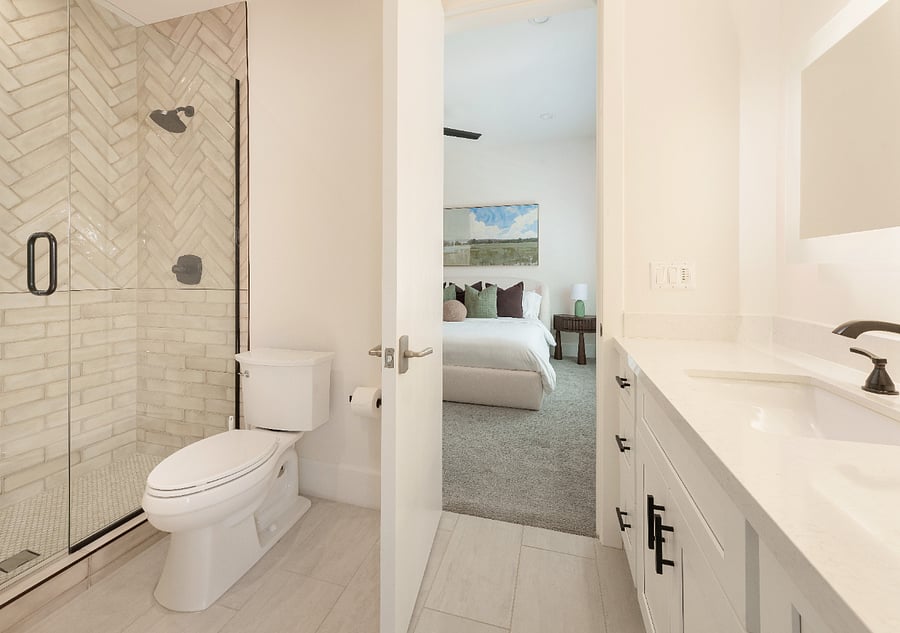 Shared full bathroom connecting both guest bedrooms, featuring a glass-enclosed shower with herringbone tile, single vanity with stone countertop, and matte black fixtures.