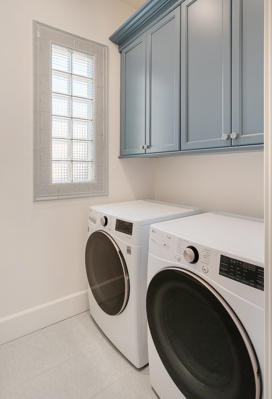 The primary ensuite includes a freestanding soaking tub, oversized glass-enclosed walk-in shower with bench and floor-to-ceiling tile, dual vanities with stone countertops and custom blue cabinetry, and a private laundry room with full-size LG washer and dryer and additional cabinetry.