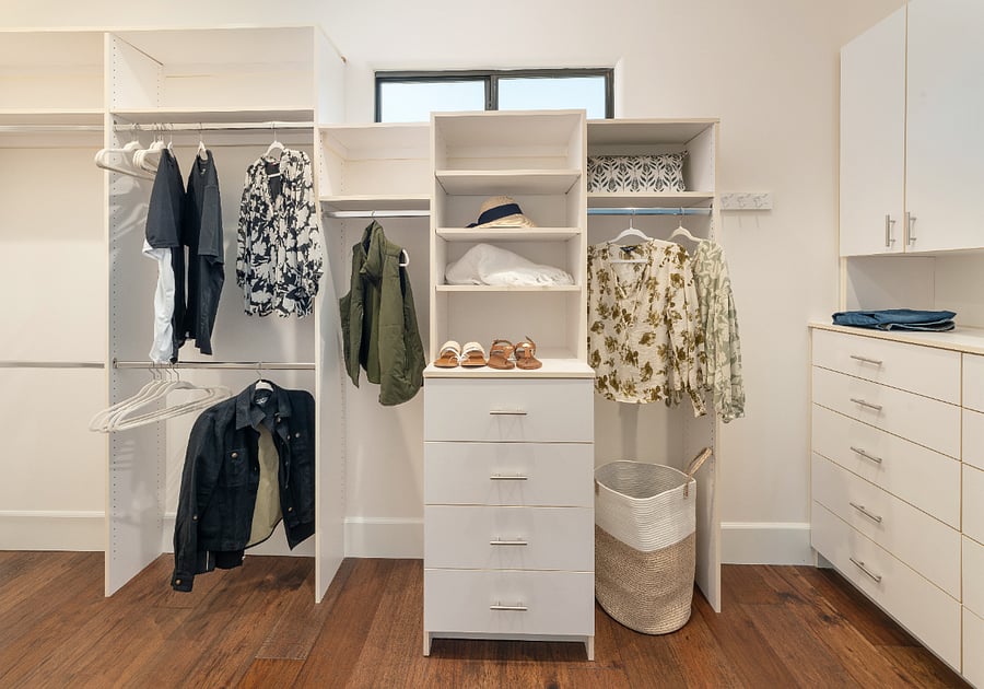Spacious walk-in closet with floor-to-ceiling built-in shelving, double hanging rods, dedicated drawer units, and hardwood floors.