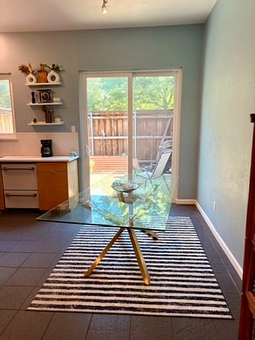 The dining room with a modern glass and gold table, which has two accompanying chairs. The backyard is behind the dining room table.