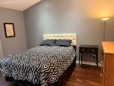 The primary bedroom has a queen size bed, a nightstand, a dimmable floor lamp, and a four drawer dresser.