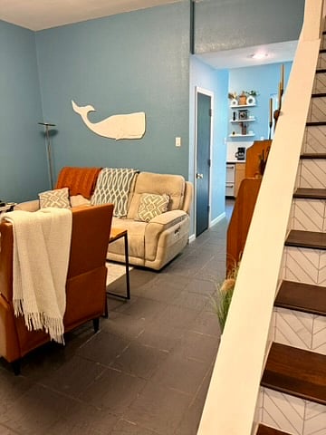 A view of the living room to the left, the kitchen in the middle of the photo, and the stairs to the second level on the right.