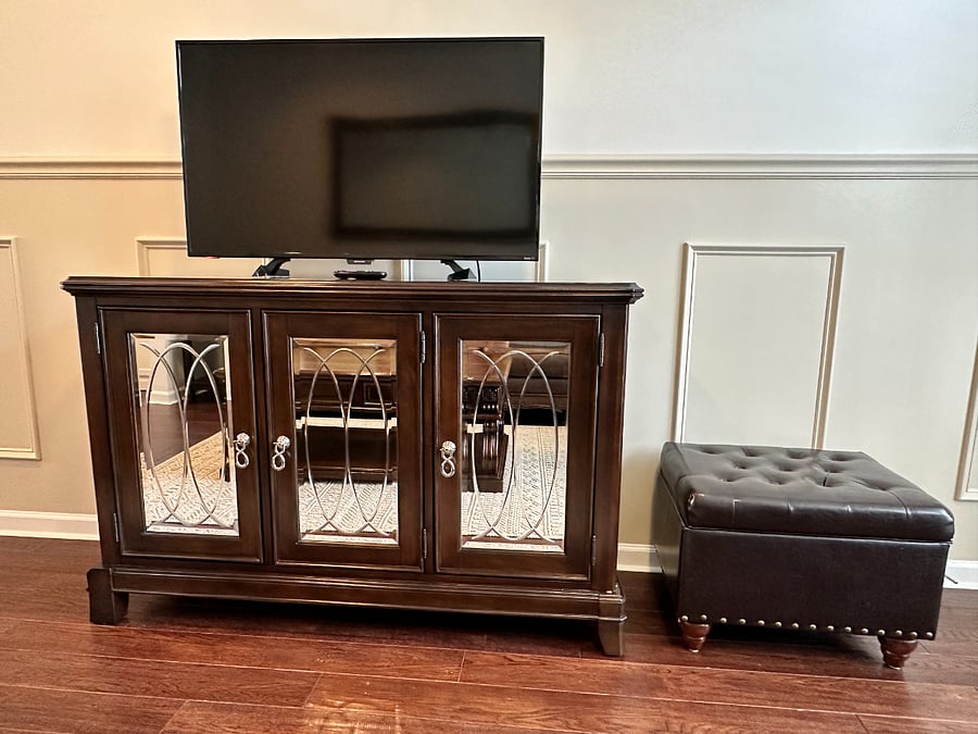 Smart TV with leather ottoman that stores blankets and TV table which has wine racks inside.