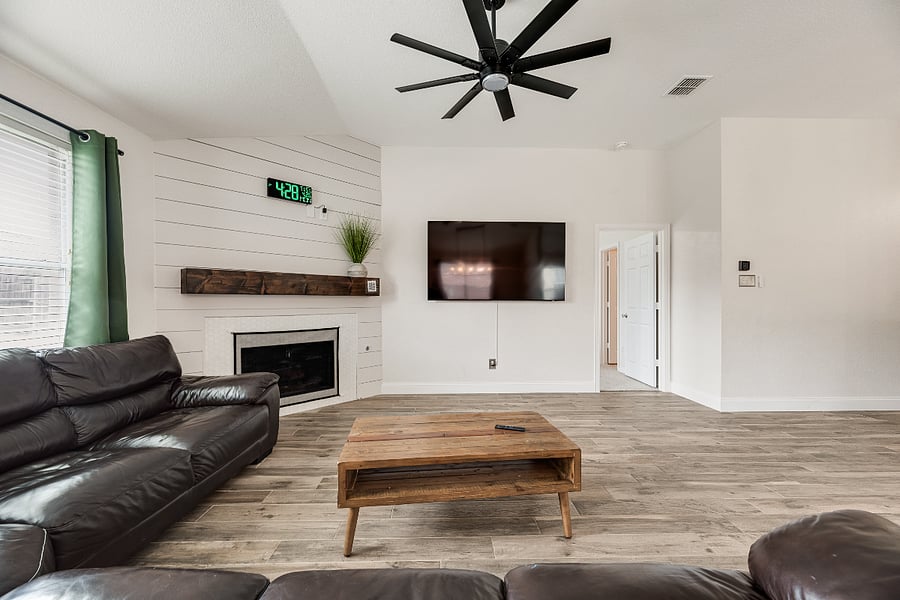 Open-concept living room featuring plush seating, a sleek 75" Smart TV and modern wall-mounted digital clock - designed for comfort and connection.