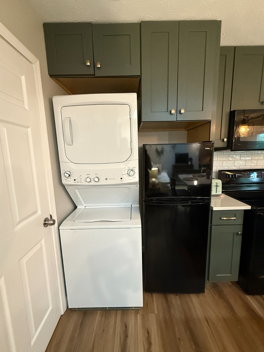 Stacked washer and dryer next to fridge with cabinet storage space