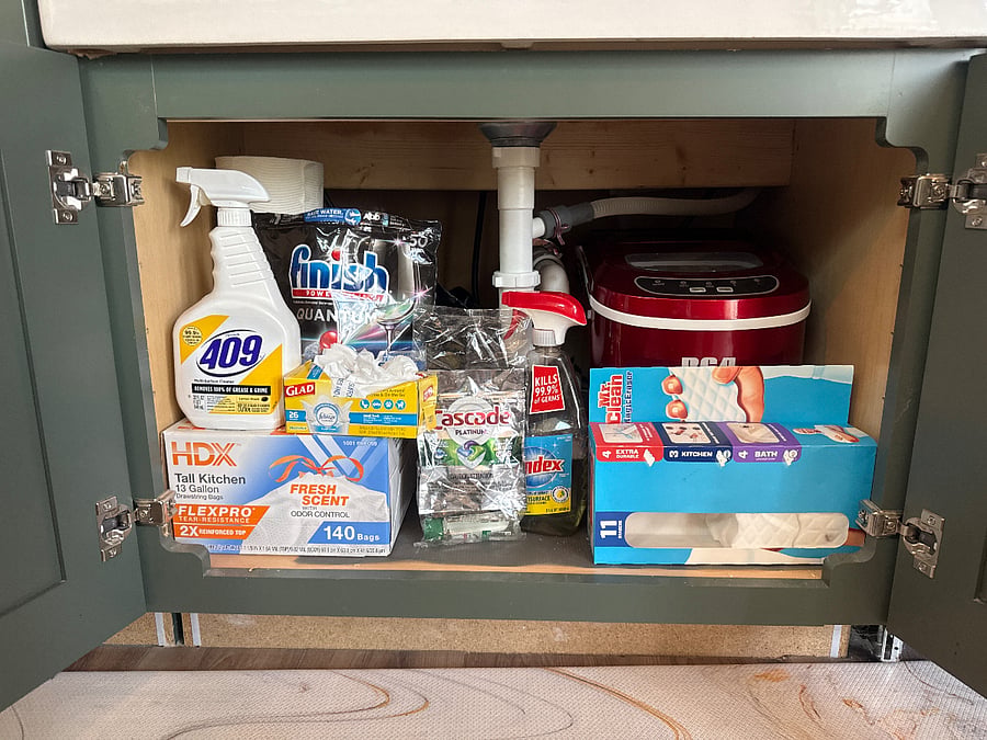 Cabinet under the sink fully stocked with cleaning supplies and an ice making machine 