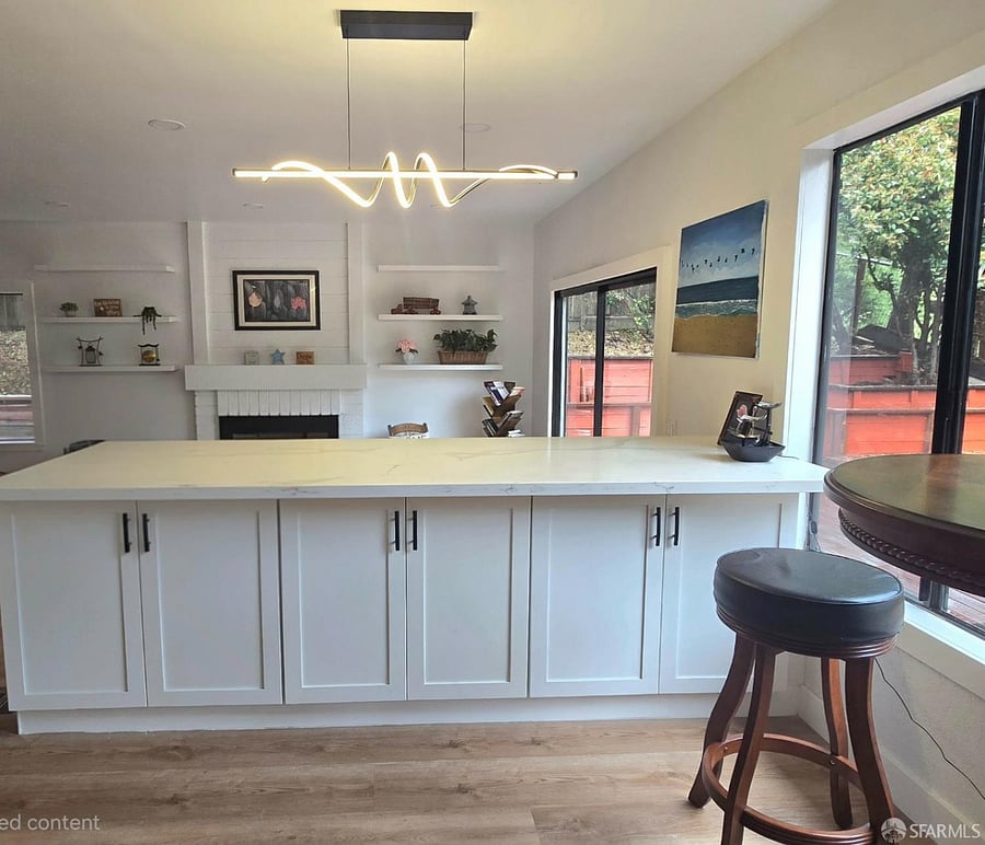 Kitchen features white countertops, island, and large window overlooking trees.