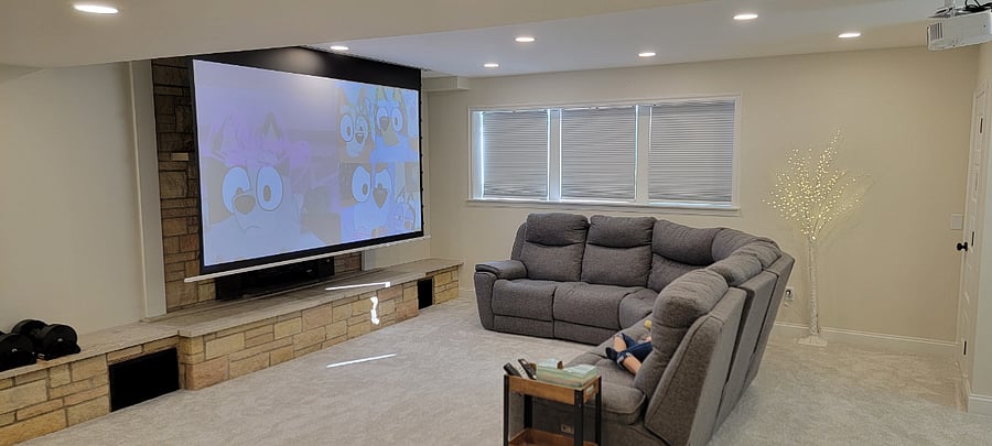 Living room with projector and blackout shades. All smart TV style set up. Also includes desk area for work at home.
