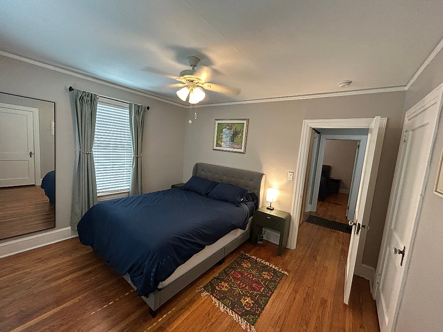 Bedroom 2 is bright, spacious, and comfortable, with multiple windows, original hardwood floors, closet space, bedside lighting, a ceiling fan, and a full-length mirror. The room has a calm, inviting feel that makes it easy for traveling professionals to relax, recharge, and feel at home.