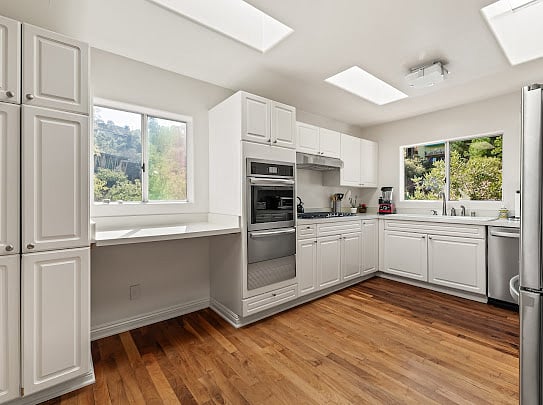 Skylit chef's kitchen with double skylights, white shaker cabinets, and stainless 6-burner range.