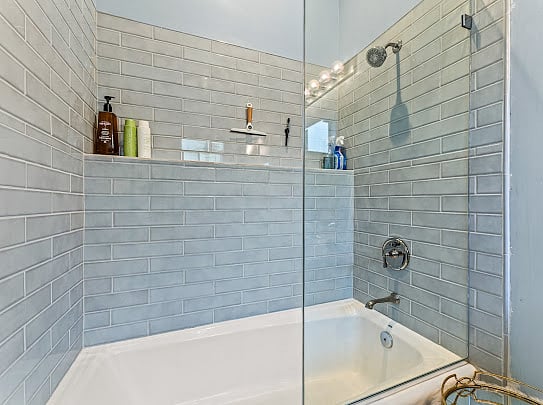 Full bathroom with walk-in shower-tub combo, light blue subway tile, and built-in toiletries niche.