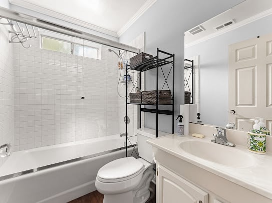 Second full bathroom with shower-tub combo, freestanding storage, and bright natural light.
