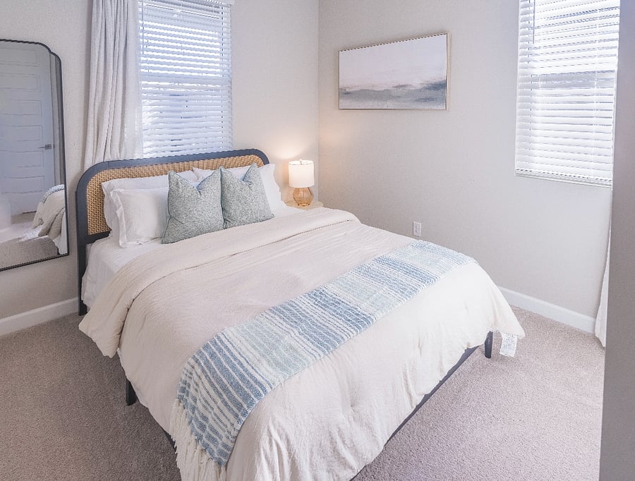 Inviting guest bedroom featuring a sleek rattan headboard, plush pillows, and a warm bedside lamp.