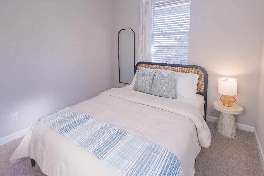 Bright and cozy guest bedroom with soft neutral bedding, modern decor, and abundant natural light.