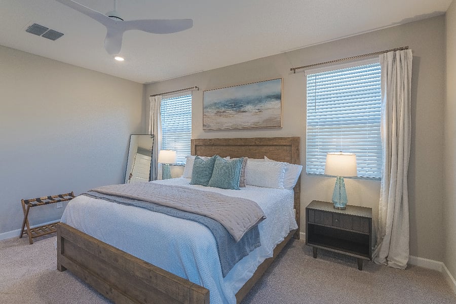 Stylish master bedroom featuring warm wood furniture, airy curtains, and a serene coastal color palette.