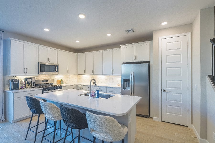 Bright modern kitchen with white cabinetry, quartz island, stainless steel appliances, and bar seating.