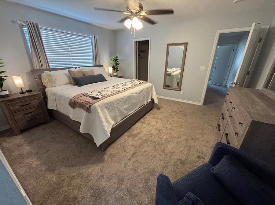 Primary bedroom featuring king bed, smart TV, walk-in closet, full-length mirror, attached bathroom with walk-in shower, and relaxing recliner.